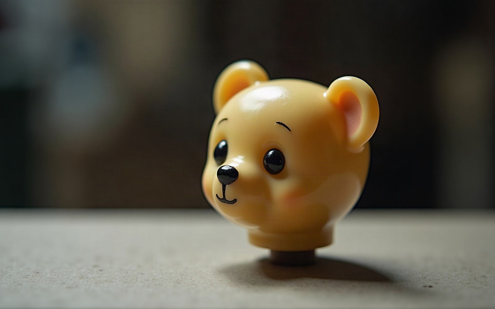 A glossy plastic bear-head toy piece with painted eyes sitting on a table