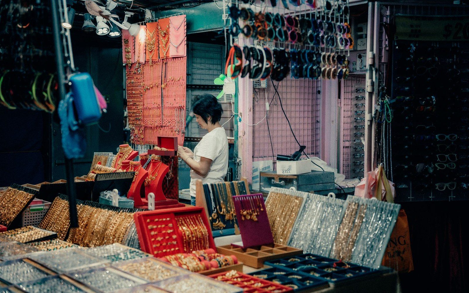 A vendor arranges necklaces at a jewelry stall lined with bracelets and sunglasses