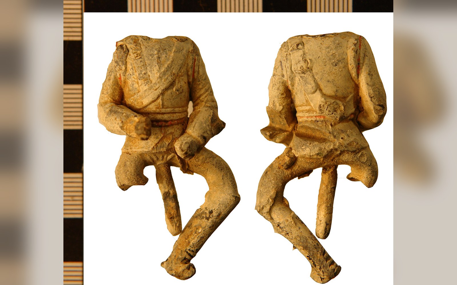 Front and back views of a headless hollow-cast lead toy soldier figurine beside a measuring scale