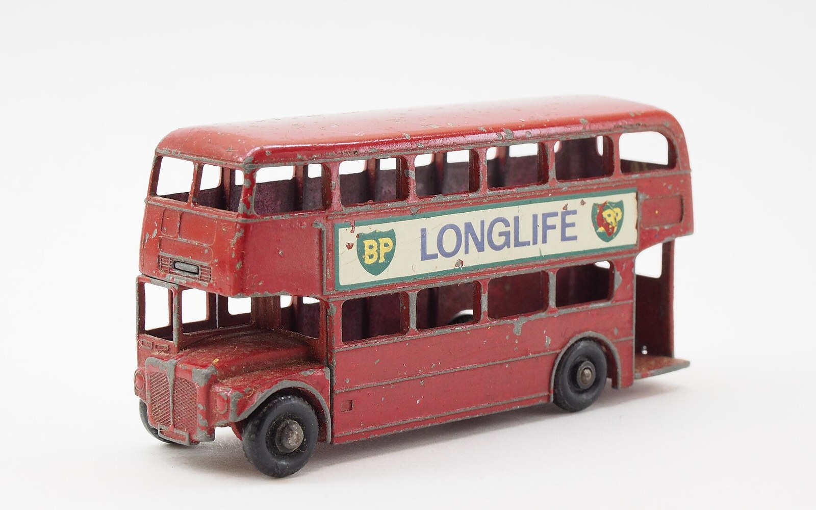 A weathered red toy double-decker bus with a "BP Longlife" advertisement on its side