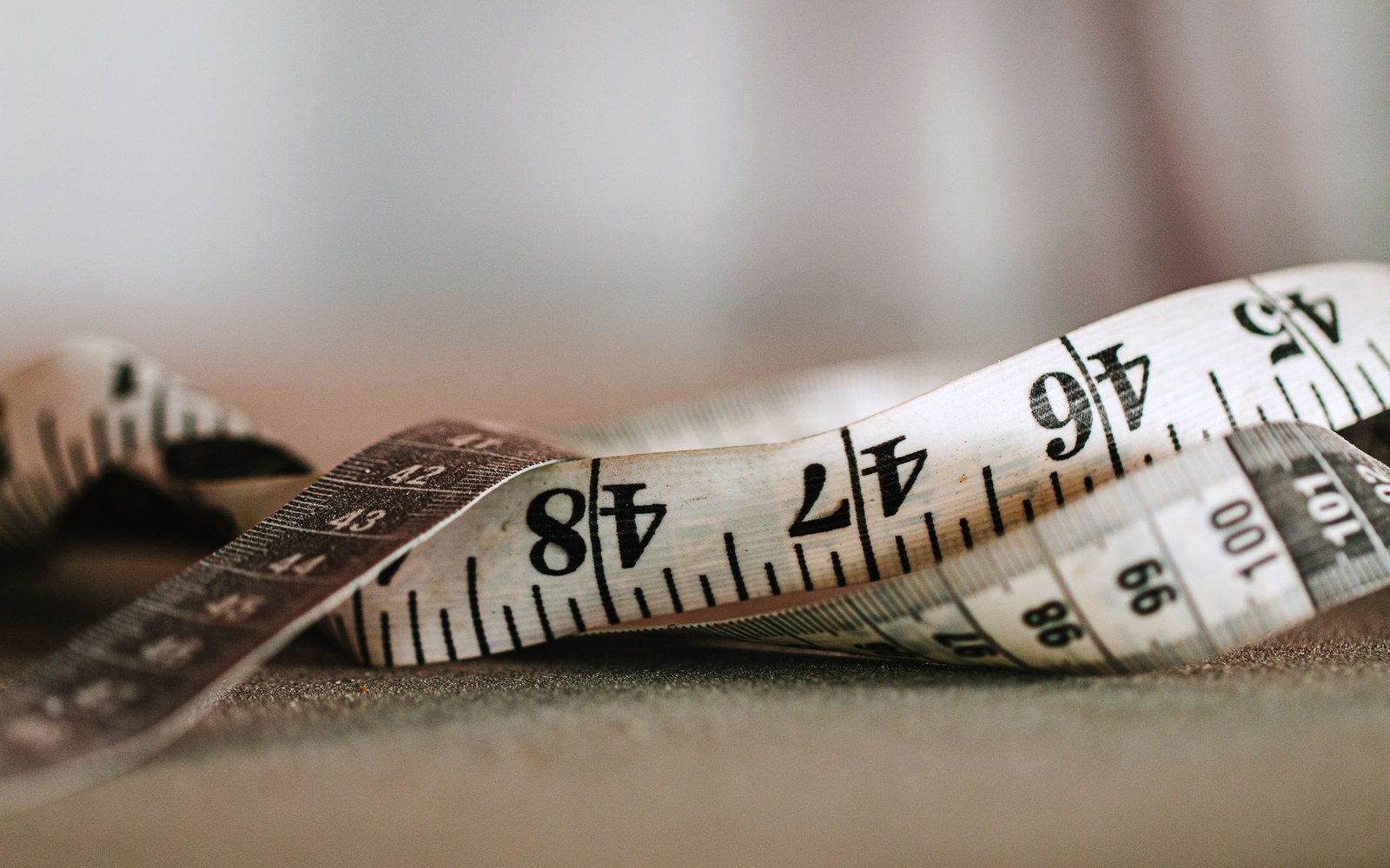 A coiled fabric tape measure showing centimeter markings resting on a textured surface
