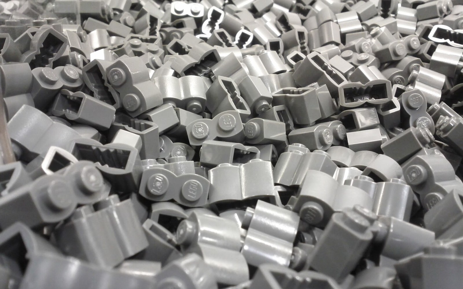 A large pile of identical light gray Lego bricks with rounded corner pieces