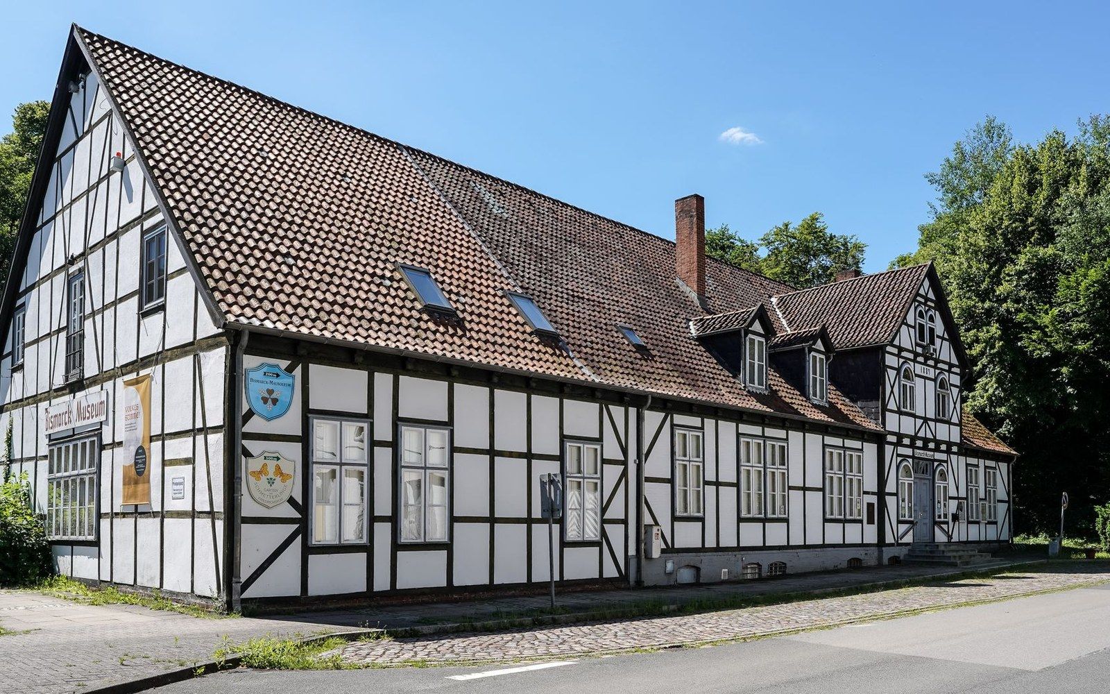 Long half-timbered farmhouse with a steep tiled roof and dormer windows along a rural road