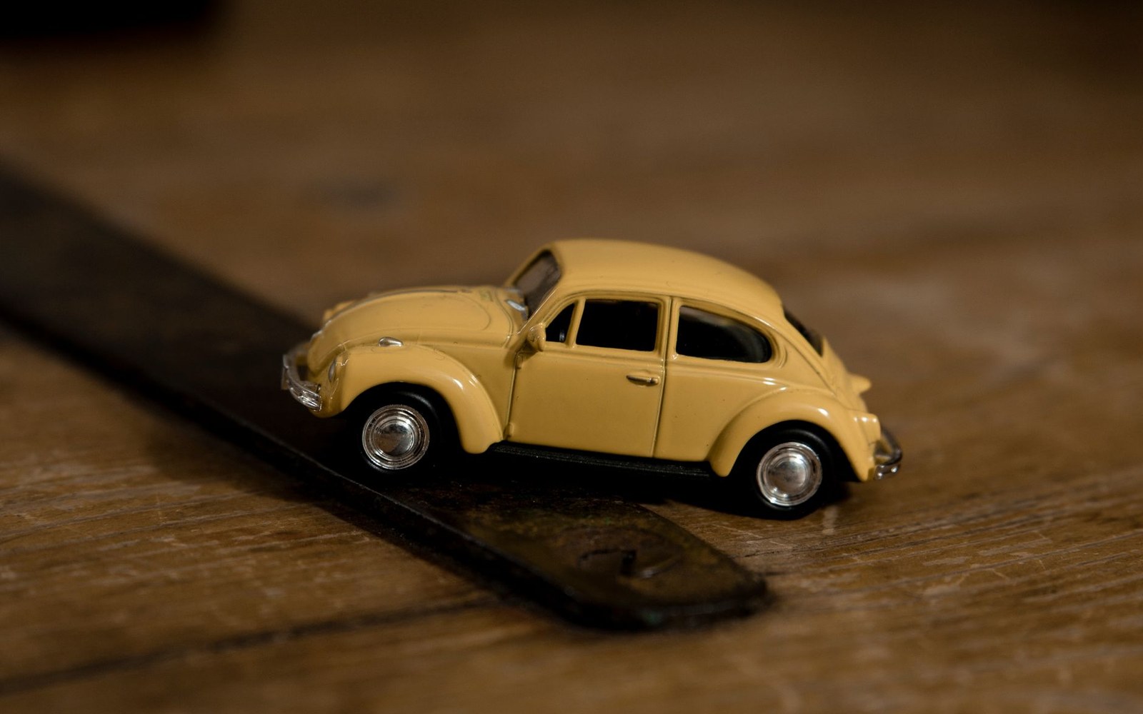 A yellow toy Volkswagen Beetle sits on a wooden floor beside a leather strap