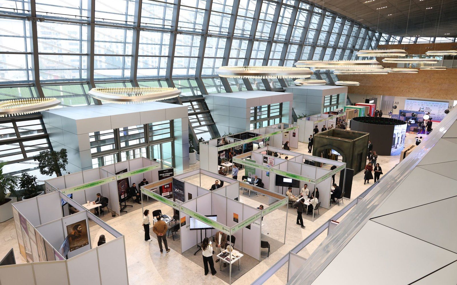 Interior of a Nuremberg Toy Fair exhibition hall, adult exhibitors and trade buyers at stands, display shelving visible in the background